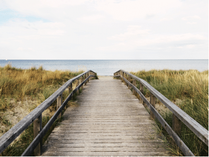 Wooden boardwalk leading to the ocean through sand dunes, symbolising the path to a dream beach house.