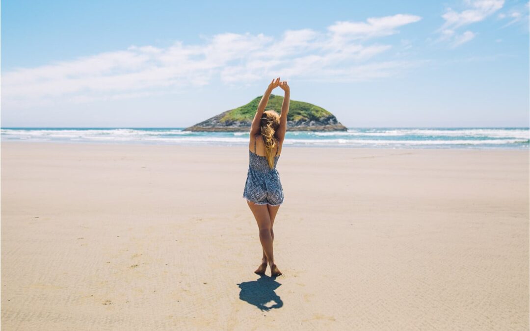 Woman stretching on a sunny beach with an island in the distance, symbolising beachside living dreams.